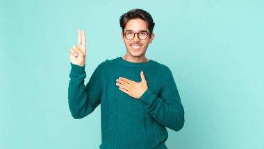 İspanyol yakışıklı adam mutlu, kendinden emin ve güvenilir görünüyor, gülümsüyor ve zafer işareti gösteriyor, olumlu bir tavırla.