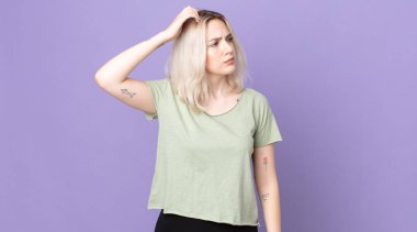 Güzel albino kadın şaşkın ve kafası karışmış hissediyor, kafasını kaşıyor ve yan tarafa bakıyor.