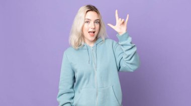 Oldukça albino bir kadın mutlu, eğlenceli, kendinden emin, pozitif ve asi hissediyor, elle kaya ya da heavy metal işareti yapıyor.