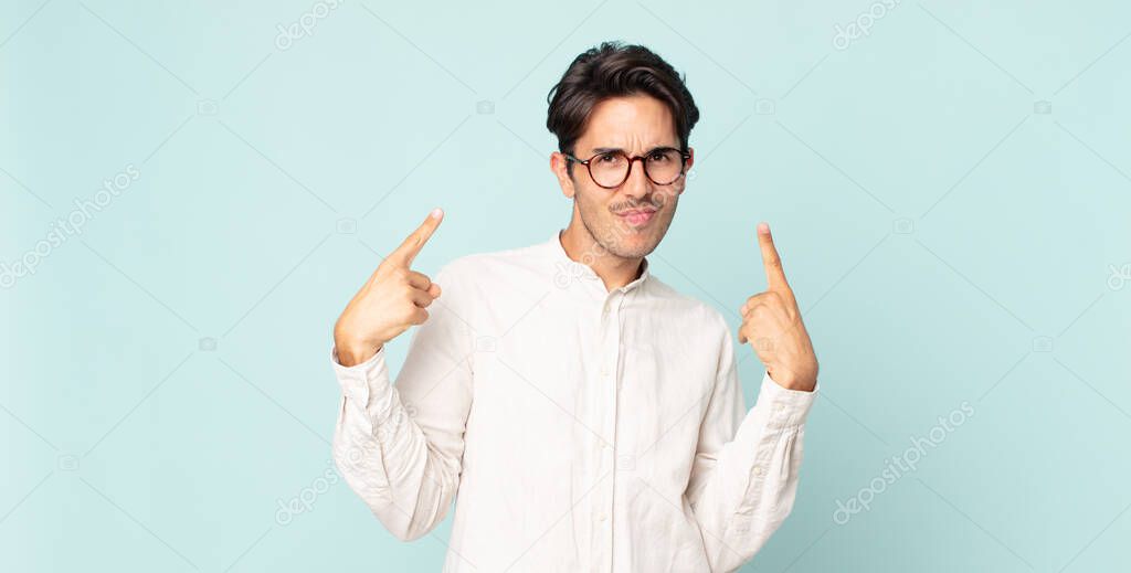 hispanic handsome man with a bad attitude looking proud and aggressive, pointing upwards or making fun sign with hands