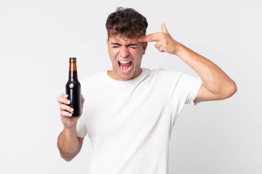 Genç ve yakışıklı adam mutsuz ve stresli görünüyor, intihar jesti silah işareti yapıyor ve elinde bira şişesi tutuyor.