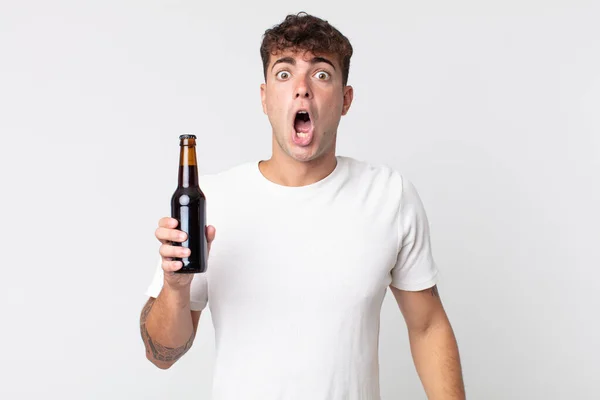 若いハンサムな男はショックを受けたり驚いたりビールボトルを持っていて — ストック写真