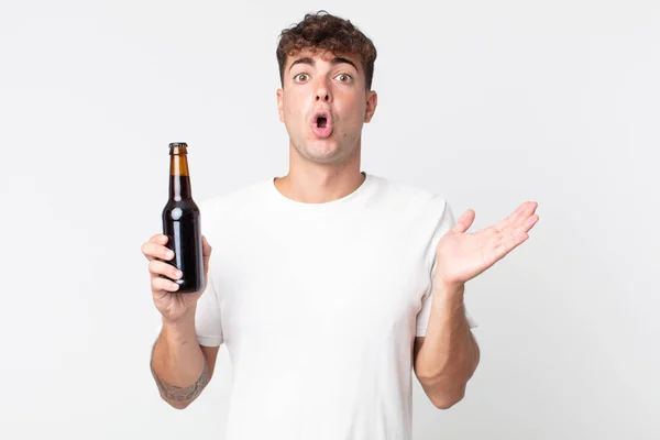 若いハンサムな男が驚いてショックを受け顎が物を持ってビール瓶を持って落下しました — ストック写真