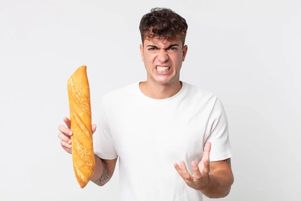 腹を立てていらいらしている若いハンサムな男パンのバゲットを持っている — ストック写真
