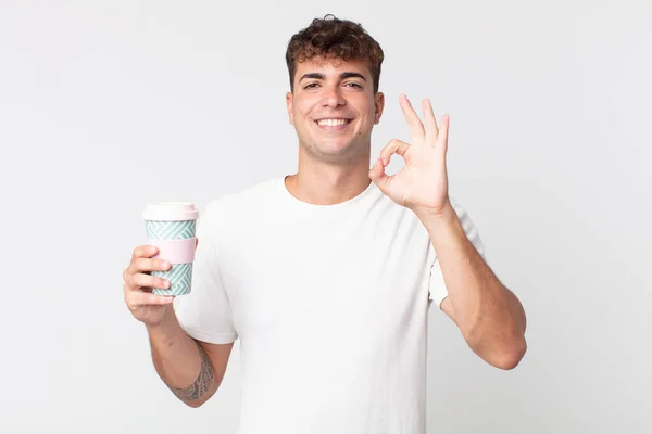 年轻英俊的男子感到快乐 以一个好的姿态表示赞同 并拿起一杯咖啡 — 图库照片