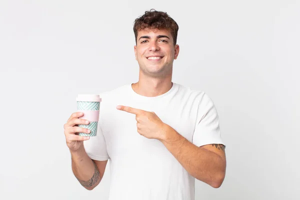 年轻英俊的男子兴高采烈地笑着 感到快乐 指着旁边 端着一杯咖啡 — 图库照片