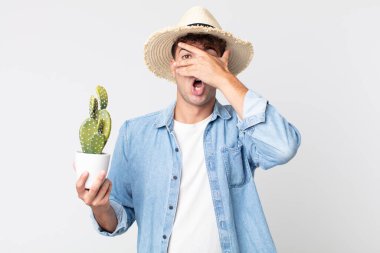 Genç, yakışıklı adam şok olmuş, korkmuş ya da korkmuş görünüyor. Elinde dekoratif kaktüs tutan çiftçi.