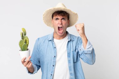 Genç yakışıklı adam sinirli bir ifadeyle agresif bir şekilde bağırıyor. Elinde dekoratif kaktüs tutan çiftçi.