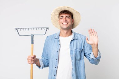 Genç yakışıklı adam mutlu bir şekilde gülümsüyor, el sallıyor, sizi selamlıyor ve selamlıyor. çiftçi kavramı