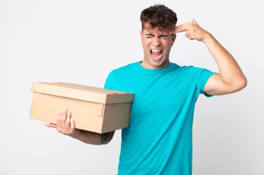 Genç yakışıklı adam mutsuz ve stresli görünüyor, intihar jesti silah işareti yapıyor ve elinde bir karton kutu tutuyor.