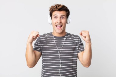 Genç yakışıklı adam şok olmuş hissediyor, gülüyor ve başarıyı kutluyor. müzik konseptini dinlemek