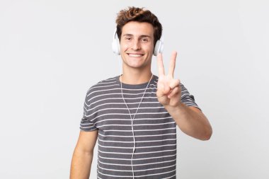 Genç yakışıklı adam gülümsüyor ve mutlu görünüyor, zafer ya da barış işareti yapıyor. müzik konseptini dinlemek