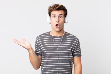 Genç, yakışıklı adam şaşırmış ve şok olmuş görünüyor. Çenesi düşmüş, elinde bir nesne var. müzik konseptini dinlemek