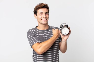 Genç yakışıklı adam kendini mutlu hissediyor ve meydan okumayla yüzleşiyor ya da kutlama yapıyor ve elinde çalar saat tutuyor.