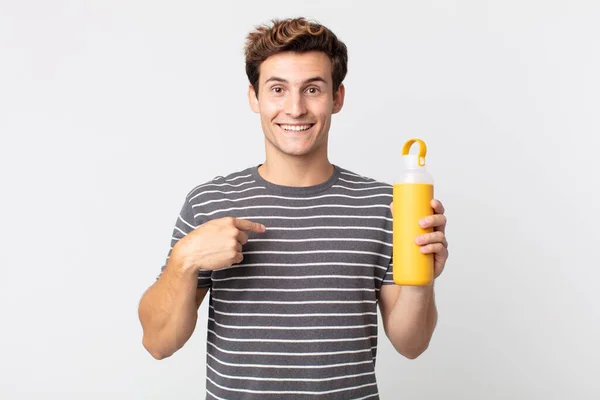 若いハンサムな男は興奮してコーヒー魔法瓶を持って自分自身を指して幸せを感じている — ストック写真