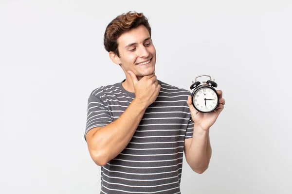 Jovem Bonito Homem Sorrindo Feliz Sonhando Acordado Duvidar Segurando Despertador — Fotografia de Stock