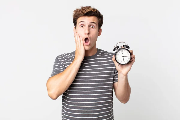 Jovem Bonito Homem Sentindo Chocado Assustado Segurando Despertador — Fotografia de Stock