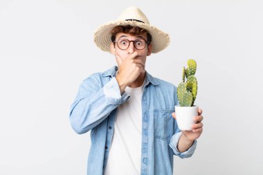 Genç ve yakışıklı bir adam elleri ile ağzını kapatıyor ve şok geçiriyor. Elinde dekoratif kaktüs tutan çiftçi.