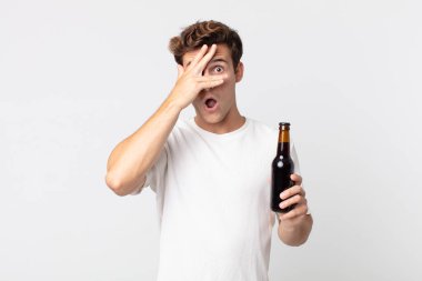 Genç, yakışıklı adam şok olmuş, korkmuş ya da korkmuş görünüyor. Yüzü elle kaplanmış ve elinde bira şişesi tutuyor.