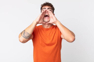 Genç yakışıklı adam mutlu, heyecanlı ve pozitif hissediyor. Elleri ağızda, bağırıyor.