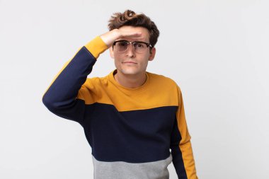 Genç yakışıklı adam şaşkın ve şaşkın bakıyor, el üstünde uzak bakıyor, izliyor ya da arıyor