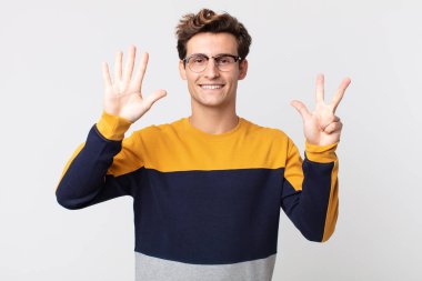 Genç yakışıklı adam gülümsüyor ve arkadaş canlısı görünüyor, 8 ya da 8 numarayı gösteriyor, eli önde, geri sayıyor.