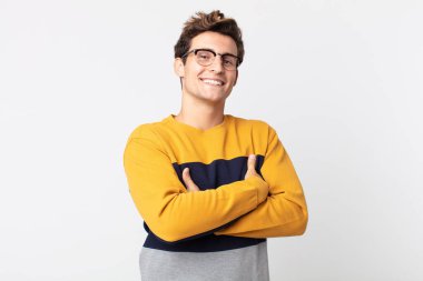 Genç yakışıklı adam kollarını kavuşturup mutlu bir şekilde gülüyor, rahat, pozitif ve tatmin edici bir pozla.