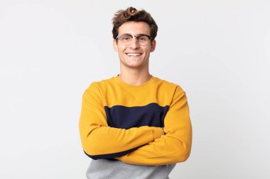 Genç yakışıklı adam mutlu, gururlu ve tatmin olmuş görünüyor. Kollarını kavuşturup gülümsüyor.