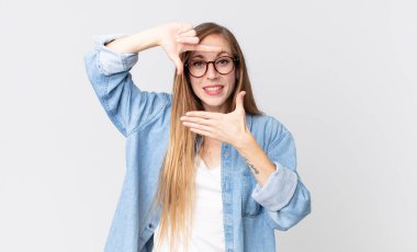 Oldukça zayıf bir kadın mutlu, arkadaş canlısı ve pozitif hissediyor, gülümsüyor ve elleriyle bir portre veya fotoğraf çerçevesi yapıyor.