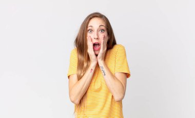 Oldukça zayıf bir kadın şok olmuş ve korkmuş hissediyor, ağzı açık ve elleri yanaklarında korkmuş görünüyor.