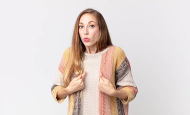 Oldukça zayıf bir kadın, şaşkın ve şaşkın bir bakışla kendini işaret ediyor, seçilmiş olmasına şaşırmış ve şaşırmış.