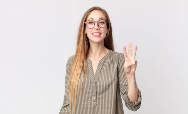 Oldukça zayıf bir kadın gülümsüyor ve arkadaş canlısı görünüyor. Üç ya da üç numarayı gösteriyor. Elleri önde ve geri sayıyor.