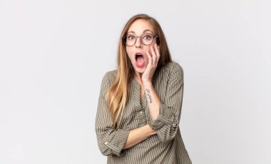 Oldukça ince bir kadın şok ve inanmazlık içinde, elleri yanağında ve kolları çaprazlanmış, sersemlemiş ve şaşırmış hissediyor.