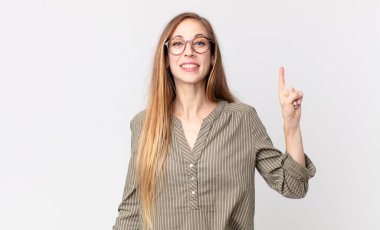 Oldukça zayıf bir kadın neşeli ve mutlu bir şekilde gülümsüyor, tek eliyle yukarıyı işaret ederek boşluğu kopyalıyor.