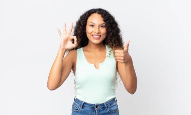 Güzel, İspanyol bir kadın mutlu, şaşkın, tatmin olmuş ve şaşırmış hissediyor, iyi olduğunu gösteriyor ve el kol hareketleri yapıyor, gülümsüyor.