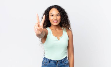 Güzel İspanyol kadın gülümsüyor ve mutlu görünüyor, kaygısız ve pozitif, zafer ya da barış işareti yapıyor.