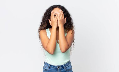 Güzel İspanyol kadın elleriyle yüzünü kapatıyor, parmaklarının arasından şaşkın bir ifadeyle yan tarafa bakıyor.