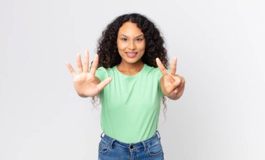 Güzel İspanyol bir kadın gülümsüyor ve dost canlısı görünüyor, 7 ya da 7 numarayı gösteriyor, eli önde, geriye doğru sayıyor.