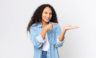 Güzel İspanyol kadın neşeyle gülümsüyor ve yan taraftaki fotokopi alanını işaret ederek bir nesneyi gösteriyor ya da reklamını yapıyor.
