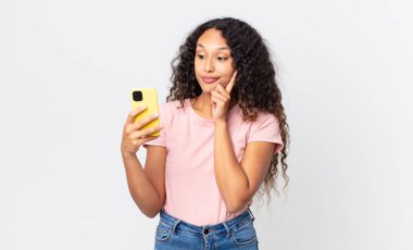 İspanyol güzel bir kadın mutlu, kendinden emin bir ifadeyle gülümsüyor. Elleri çenesinde ve elinde akıllı bir telefonla.