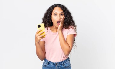İspanyol güzel kadın şok olmuş, korkmuş ve elinde bir akıllı telefon tutuyor.