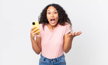 İspanyol güzel kadın inanılmaz bir sürprizle şaşkın, şaşkın ve afallamış ve elinde akıllı bir telefon tutuyor.