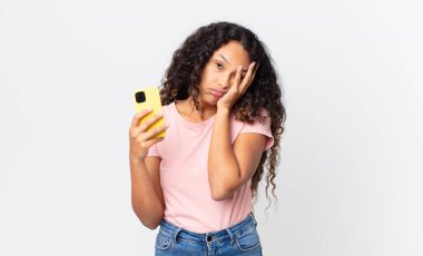 İspanyol güzel kadın sıkılmış, hayal kırıklığına uğramış ve uykulu hissediyor ve elinde akıllı bir telefon tutuyor.