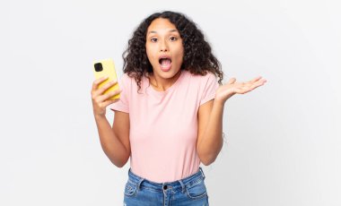 İspanyol güzel kadın şok olmuş, şaşırmış ve elinde bir akıllı telefon tutuyor.