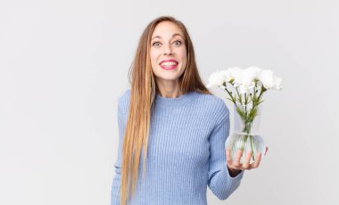 Zayıf, güzel bir kadın. Mutlu görünüyor ve hoş bir şekilde şaşırmış ve elinde Çiçeklerle vazo tutuyor.