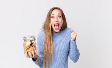 Zayıf, güzel bir kadın şoke olmuş, gülüyor, başarıyı kutluyor ve elinde kurabiye tutuyor.