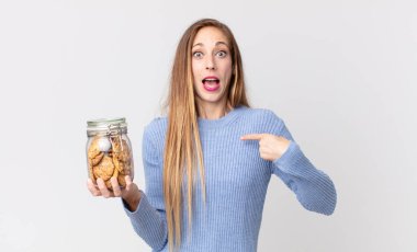 Zayıf, güzel bir kadın mutlu hissediyor ve heyecanlı ve elinde kurabiyelerle kendini işaret ediyor.