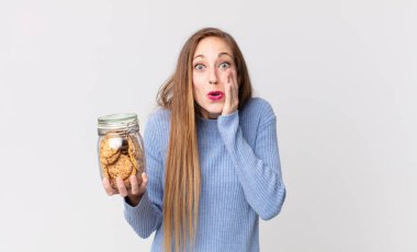 Zayıf, güzel bir kadın şok olmuş, korkmuş ve elinde kurabiye tutuyor.