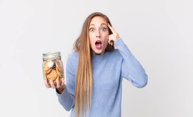 Zayıf, güzel bir kadın şaşırmış görünüyor, yeni bir düşünce, fikir ya da konsept fark ediyor ve elinde bir kurabiye tutuyor.