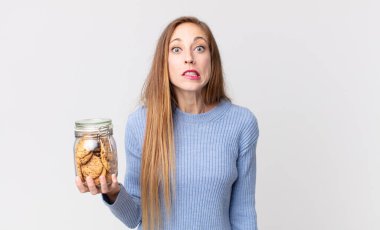 Şaşkın, kafası karışmış ve elinde kurabiye tutan ince, güzel bir kadın.